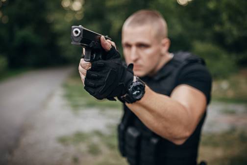 Man holding a gun, in a black vest and gloves. The image is likely related to police shootings and legal topics.